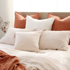 a bed with orange and white pillows on it's headboard in front of a window