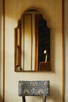 an ornate mirror hangs on the wall above a wooden bench with a patterned upholstered seat