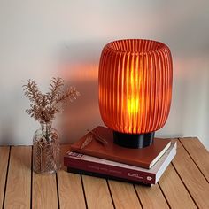 an orange lamp sitting on top of a wooden table next to a book and vase