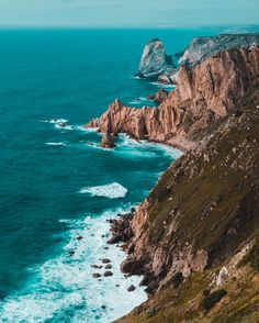 the ocean is blue and green with waves crashing against the rocky cliffs on either side