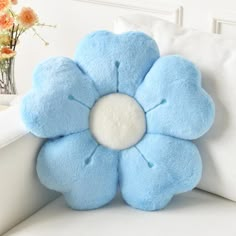 a blue flower shaped pillow sitting on top of a white couch next to a vase with flowers