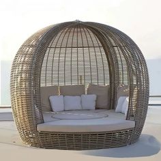 a round wicker couch with pillows on it's sides and an umbrella like structure in the middle