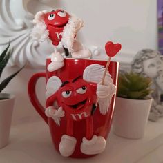 two red mugs with faces and hearts on them, one is holding a candy cane