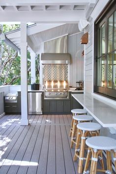 an outdoor kitchen with bar stools on the front porch and grill in the back