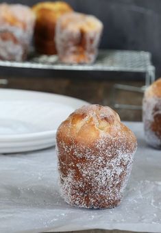 powdered sugar covered muffins sitting on top of a table next to a plate