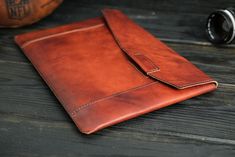 a brown leather ipad case sitting on top of a wooden table next to a camera