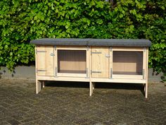 a wooden cabinet sitting next to a bush with two doors on it's sides