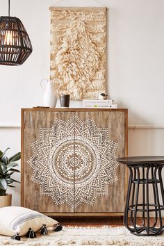 a wooden cabinet with an intricate design painted on the front and side, next to two stools