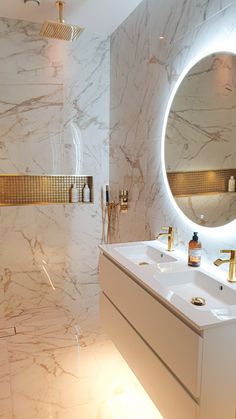 a bathroom with two sinks and a large round mirror above the sink is illuminated by lights