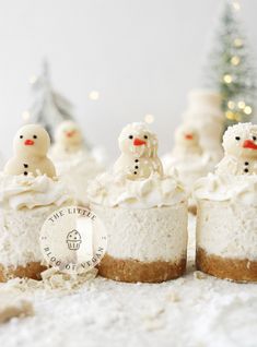 three mini snowmen sitting on top of some cheesecakes in front of a christmas tree