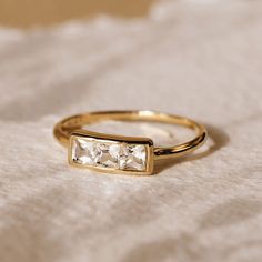 a gold ring with two princess cut diamonds on it's sides, sitting on a white cloth