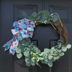 a wreath on the front door is decorated with blue flowers and green leaves as well as a red bow