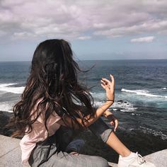 a woman sitting on the edge of a cliff looking at the ocean