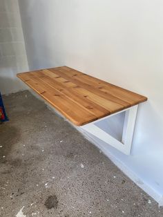 a wooden table sitting in the corner of a room next to a white wall and cement floor