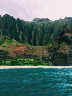 the ocean is blue and green as it sits in front of a large mountain range