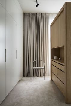 a chair sitting in front of a window next to a cabinet and cupboard with curtains on it