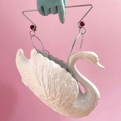 a white swan hanging from a hook with two hands on it's back and one hand holding something in the air