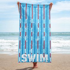 a person standing on the beach holding up a blue towel with red and white stripes