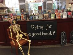 a skeleton sitting on a chair in front of a book store with a sign saying dying for a good book?