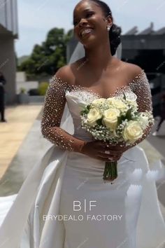 a woman in a white wedding gown holding a bouquet of flowers and smiling at the camera