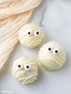 three white chocolate covered donuts with googly eyes sitting on top of a marble counter