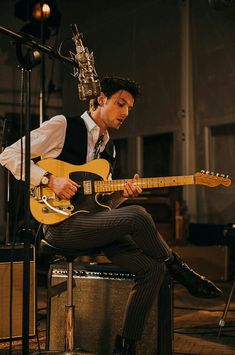 a man sitting on top of a chair playing an electric guitar in front of a microphone