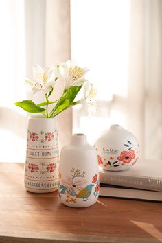 two vases with flowers in them sitting on a table next to a book and window