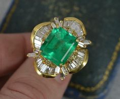 a close up of a person's hand holding an emerald and diamond ring