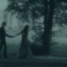 a man and woman holding hands in front of a large building on a foggy day