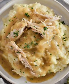 a white plate topped with mashed potatoes covered in gravy and garnished with parsley