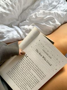 a person laying in bed reading a book with their feet up on the edge of an open book