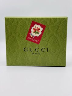 a green gucci box with a red bow on it's side and the words gucci beauty written in cursive writing