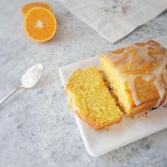 a slice of orange cake with icing on a plate next to an orange wedge