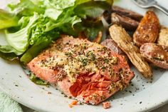 a white plate topped with salmon, potatoes and lettuce next to a salad