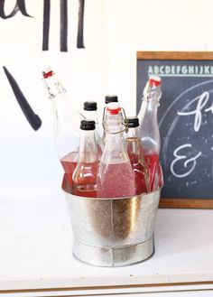 three bottles of soda sit in a bucket next to a chalkboard with writing on it