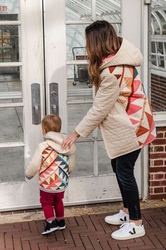 a woman holding the hand of a small child who is wearing a backpack and standing in front of a door