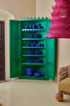 a green cabinet with blue bowls and baskets in it next to a pink lamp shade