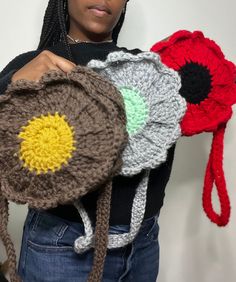 a woman is holding two crocheted hats in her hands and one has a flower on it