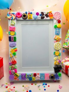 a white frame surrounded by balloons, confetti and candies on a table