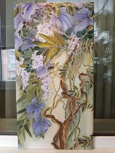 a painting with purple flowers and green leaves on a white surface next to a window