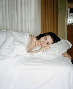 a woman laying in bed with white sheets