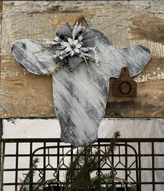 a wooden moose head decorated with flowers on top of a metal fence next to a potted plant