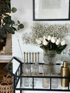 a vase filled with white flowers sitting on top of a shelf next to bottles and glasses