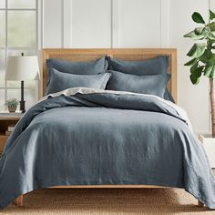 a bed with green linens and pillows in a white room next to a potted plant