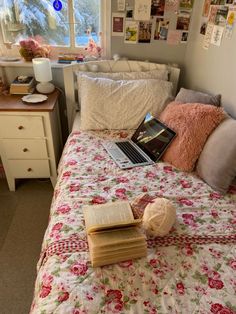 a laptop computer sitting on top of a bed next to a pile of books and pillows