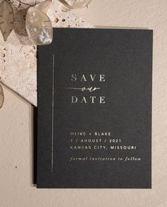 a black and gold save the date card on top of a table with some flowers