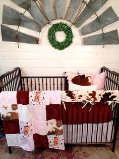 a baby crib with a cow print blanket on it and a wreath above the crib