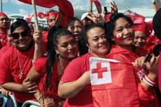 a group of women in red shirts and white crosses on their faces, some holding flags