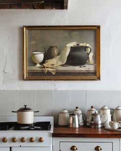 a painting hanging on the wall above a stove with pots and pans sitting on it