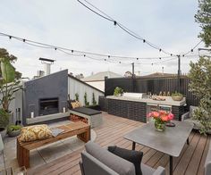 an outdoor patio with tables, couches and grill on the back deck is lit by string lights